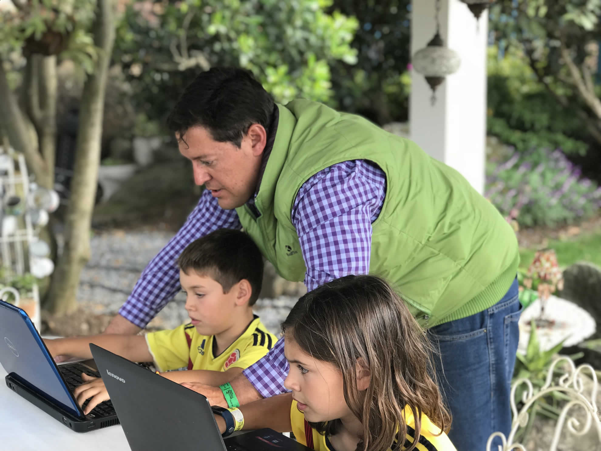 Orlando Javier Jaramillo acompaña a dos niños que programan en portátiles al aire libre