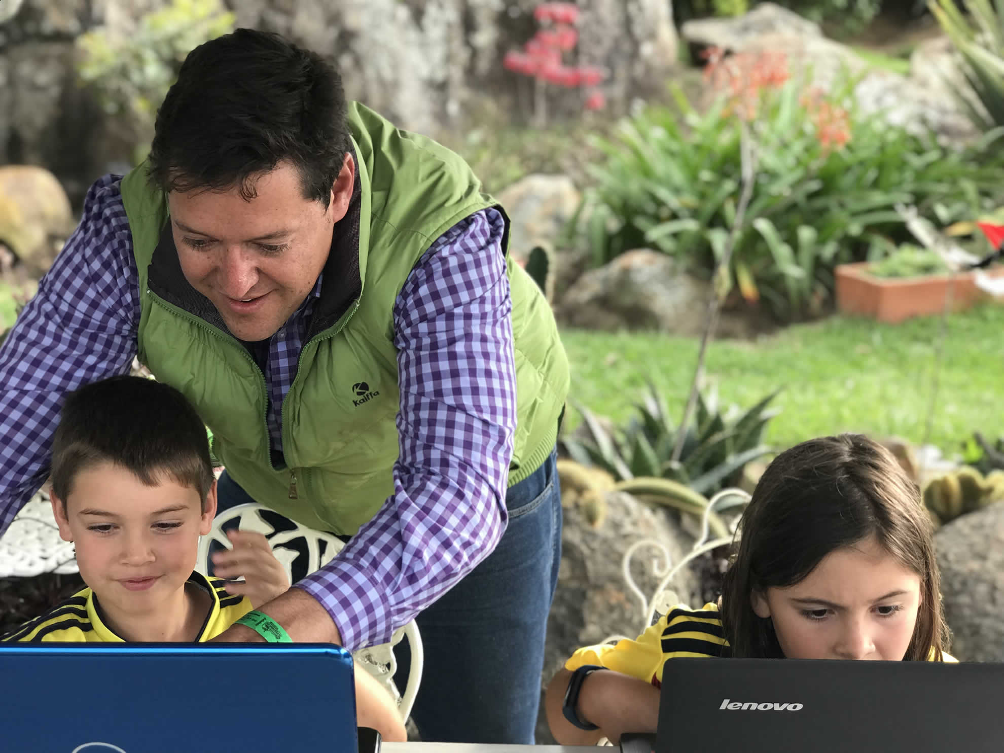 Orlando Javier Jaramillo sonríe mientras acompaña a un niño y una niña escribiendo código