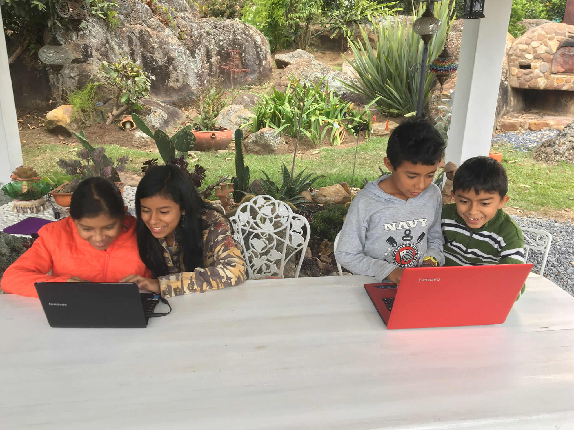 Cuatro niños y niñas programan juntos en portátiles alrededor de una mesa en un jardín